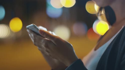 Close-up shot of Attractive Woman using Mobile Phone During Walk on Streets of Night Town