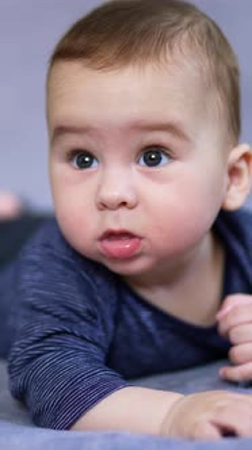 Lovely baby boy lies on belly looking up with surprise.