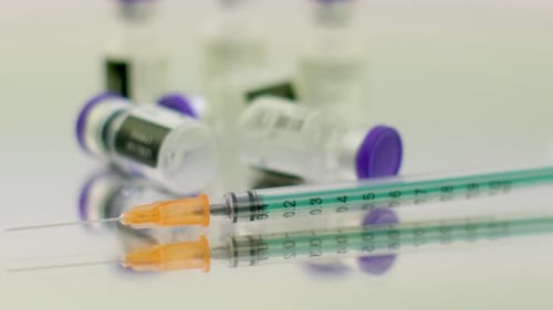 Close-up of a green syringe and a few coronavirus vaccine bottles