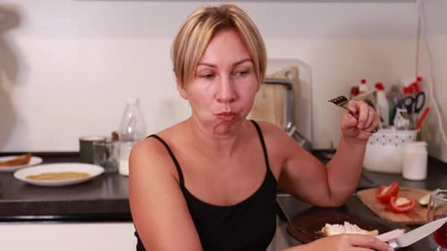 Caucasian Woman Enjoys Tasty Homemade Meal in Bright Kitchen While Preparing Ingredients