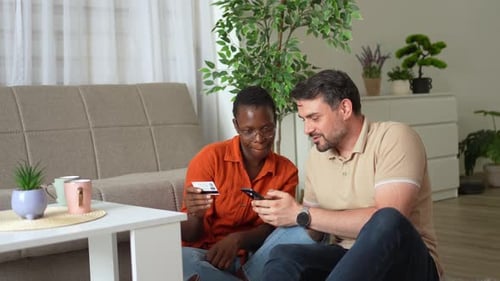 Couple sitting on floor using phone and credit card