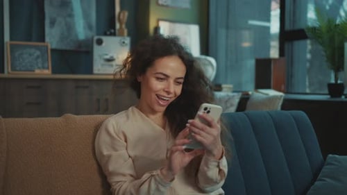 Smiling woman sitting on sofa, looking at her phone