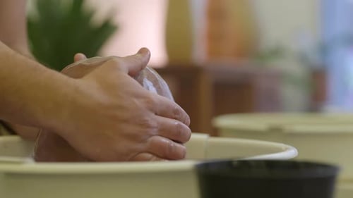 Male craftsman hands wet raw clay material on studio pottery wheel close up shot