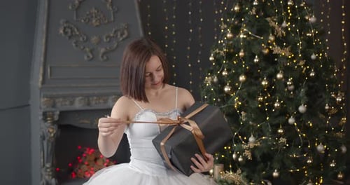 Excited Woman Opening Christmas Present by Fireplace