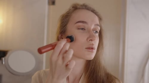 Woman Applies Makeup with Brush in Bathroom Mirror