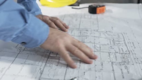Man reads blueprints at table in new home analyzing architectural plans