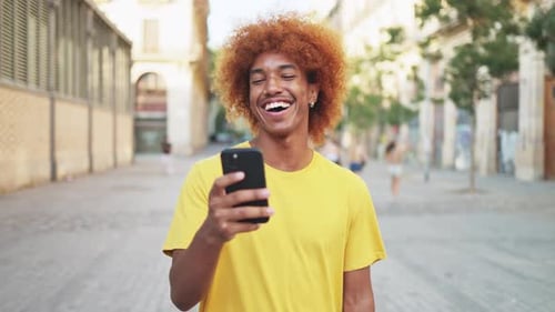 Young man happy surfing social media with his smartphone on the city street.