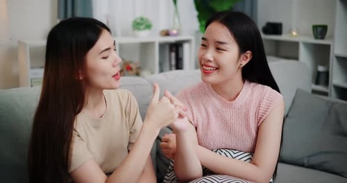 Two young women are talking and laughing happily as they spend time together on a sofa