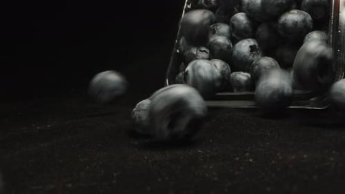 Blueberry berries pour out of the tray on a black cloth, close-up, slow-motion