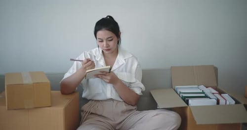 Woman Writing in Notebook with Shipping Boxes