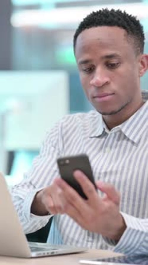 Young Adult Uses Smartphone and Laptop at Desk