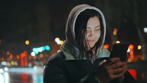 Young Pretty Woman Text Messaging on Her Smart Phone in City Street at Night