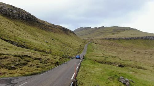 Blue car driving on a rural road in Faroe Islands