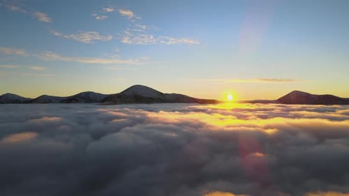 Aerial View of Vibrant Sunrise Over White Dense Clouds with Distant Dark Mountains on Horizon