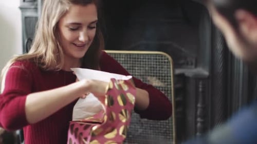 Woman Opening a Gift Near a Fireplace Indoors