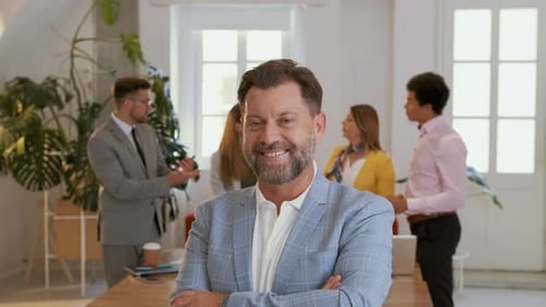 Portrait of smiling businessman in office with his colleagues in background.