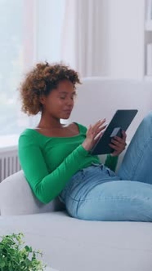Jeune femme détendue allongée sur une tablette de lecture sur un canapé dans un salon moderne et lumineux