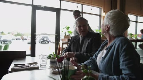 Daughter Arriving Greeting And Hugging Senior Parents In Cafe