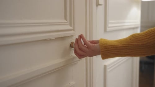 Close up shot of female hands rotating door knob before opening a white door in a house.
