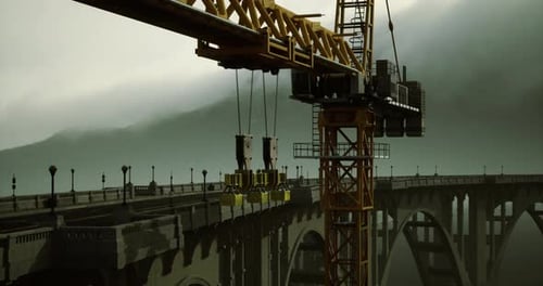 La construcción de un gran puente se desarrolla con un telón de fondo brumoso al amanecer