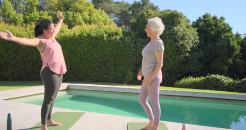 Mujeres mayores calentándose en colchonetas con botellas de agua, estirándose, dándose un paso, saludando, abrazándose junto a la piscina