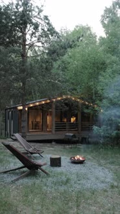 Vertical Video A Cozy Cabin Retreat with a Campfire Set in a Serene and Picturesque Forest Setting