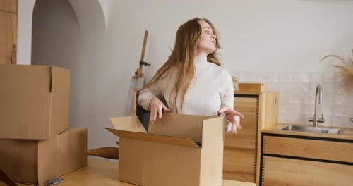 Focused Blonde Girl Putting Home Decoration Items Into Cardboard Box While Doing Home Moving