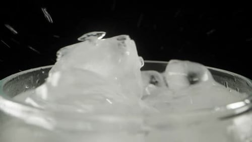 I throw an ice cube into a soda glass, on a black background, slow motion