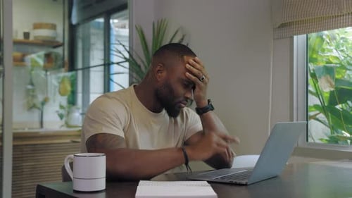 Worried Man Using Laptop at Indoor Table