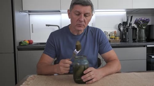 Man Eating Pickled Cucumber From Jar at Home Kitchen