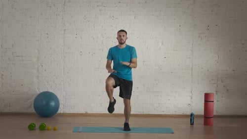 Männlicher Fitnesstrainer in Sportbekleidung macht hohe Sprünge, Cardio-Aufwärmübungen für den Online-Kurs im Heimstudio