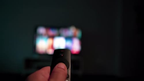 Hand Navigating TV Remote in Dimly Lit Room