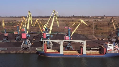 Porto marítimo com um navio ocioso e guindastes com pilhas de carvão