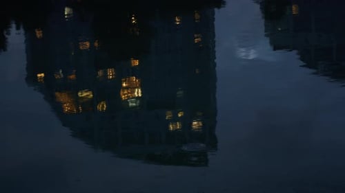 Night city buildings reflecting in calm water ripples drone view