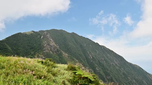 Blue sky, white clouds, the top of the mountain is covered with green grass.