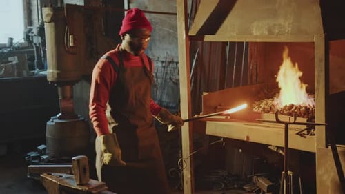 Schmied hämmert Metallstab, beheizt in der Schmiede in der Werkstatt