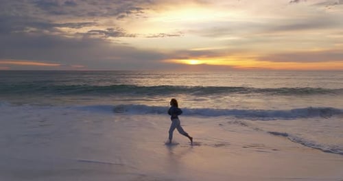 Silhouette of a Woman Running Along the Ocean Coast Barefoot on a Breaking Wave at Sunset The