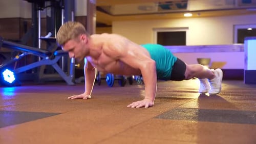 young male shirtless bodybuilder doing push-ups from the floor in a sports club or gym. Strong