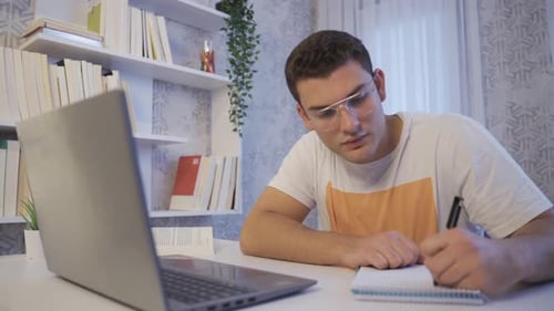 Young Man Working on Laptop and Taking Notes