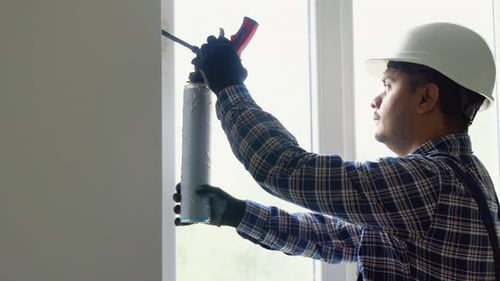 Tradesman Applying Insulation Around Window Frame