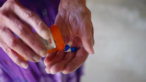 An aging woman taking her medication drug pills from a bottle into her hand.