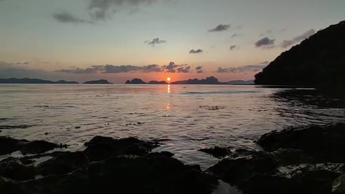 The Sun setting over the horizon, the waves crashing against rocks along the beach. The video may al