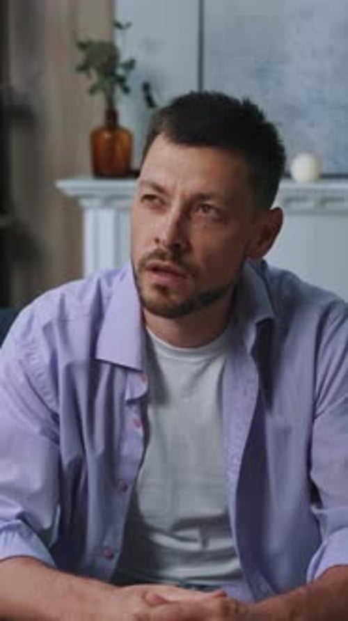 A Reflective Man Dressed Casually is Sitting Comfortably on a Couch in a Cozy Environment