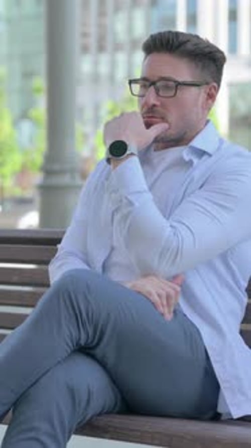 Man in Glasses Sits Contemplatively on Park Bench