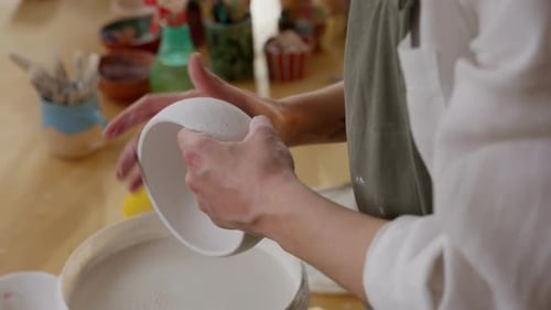 Artisan Perfecting a White Ceramic Bowl with Focused Precision in Colorful Pottery Workshop