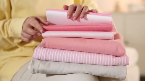 Woman with stack of clothes on sofa indoors, closeup