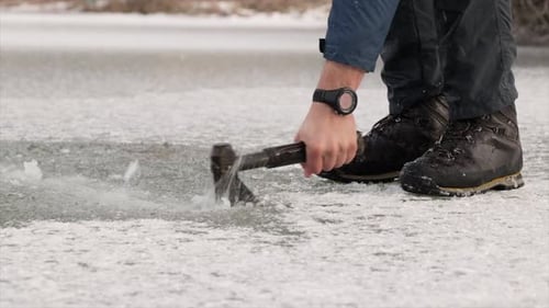 Fisherman breaking ice with an axe on a frozen lake in winter. Ice fishing.