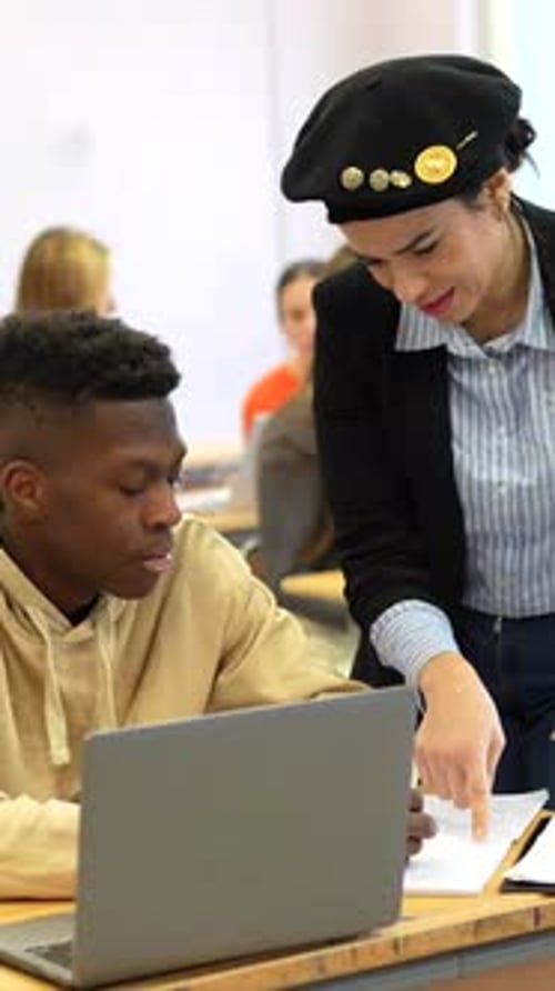 Teacher Assisting Student in Classroom with Laptop