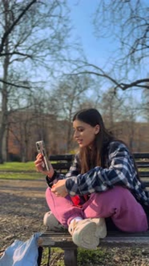 A Stunning Young Lady Speaks on the Phone While Resting on a Bench in the Park
