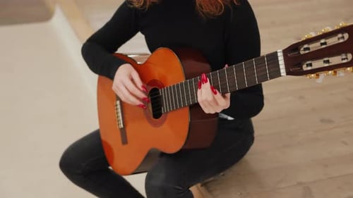 Close-up video of a woman playing chords on an acoustic guitar while sitting on stage in a room.